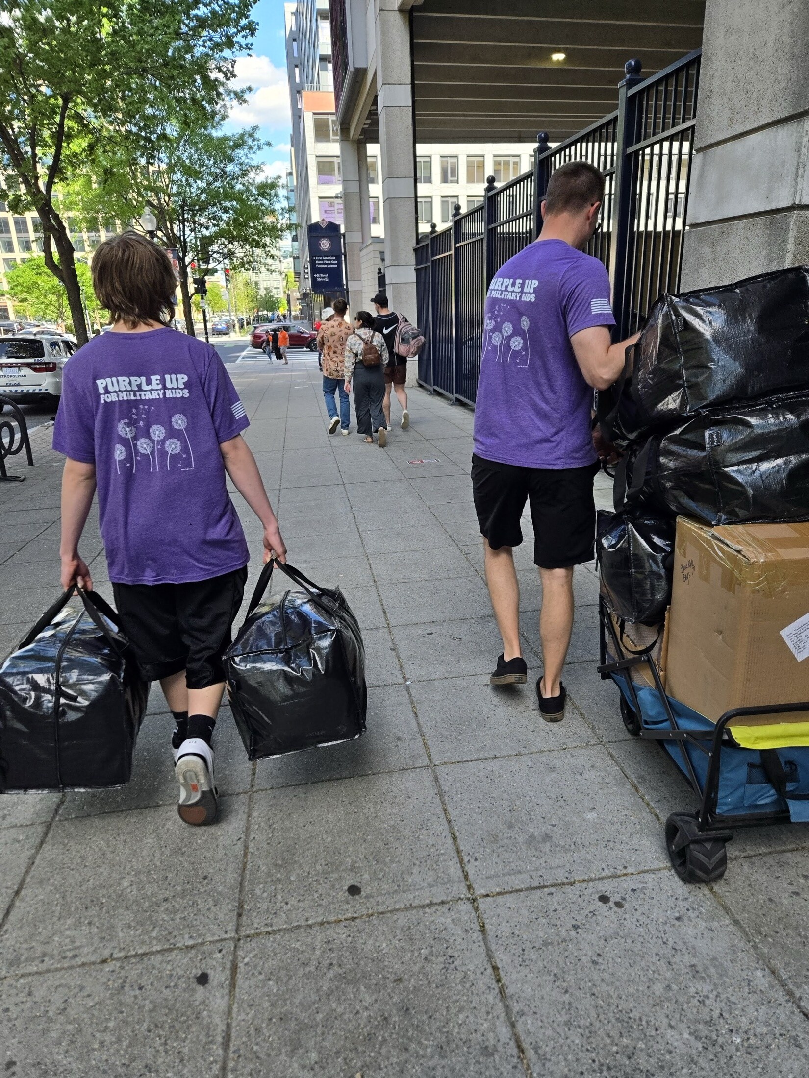 Purple Up volunteers carrying large event supply bags on a city sidewalk